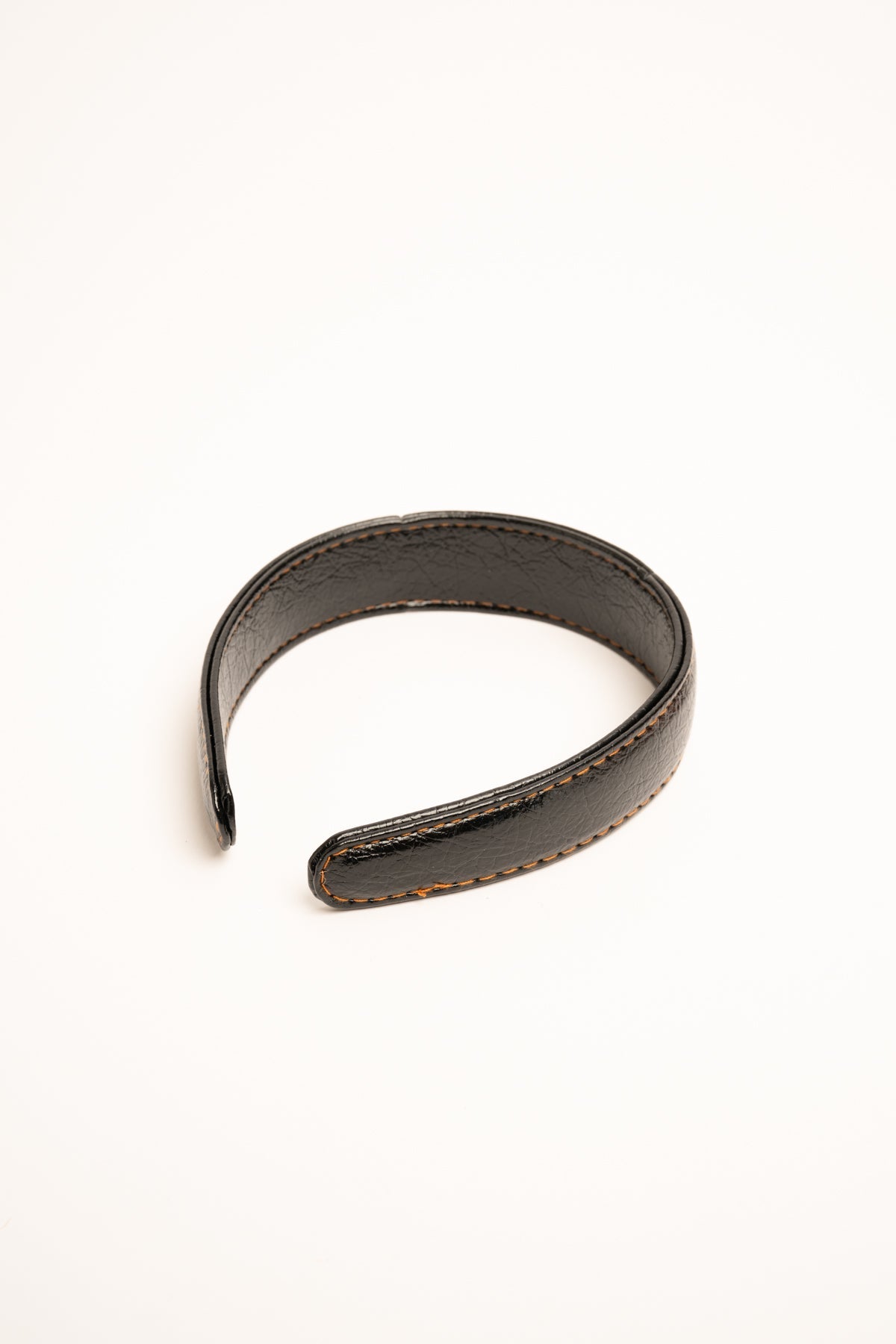 Diadema de polipiel negra con costuras naranjas y borde cosido.