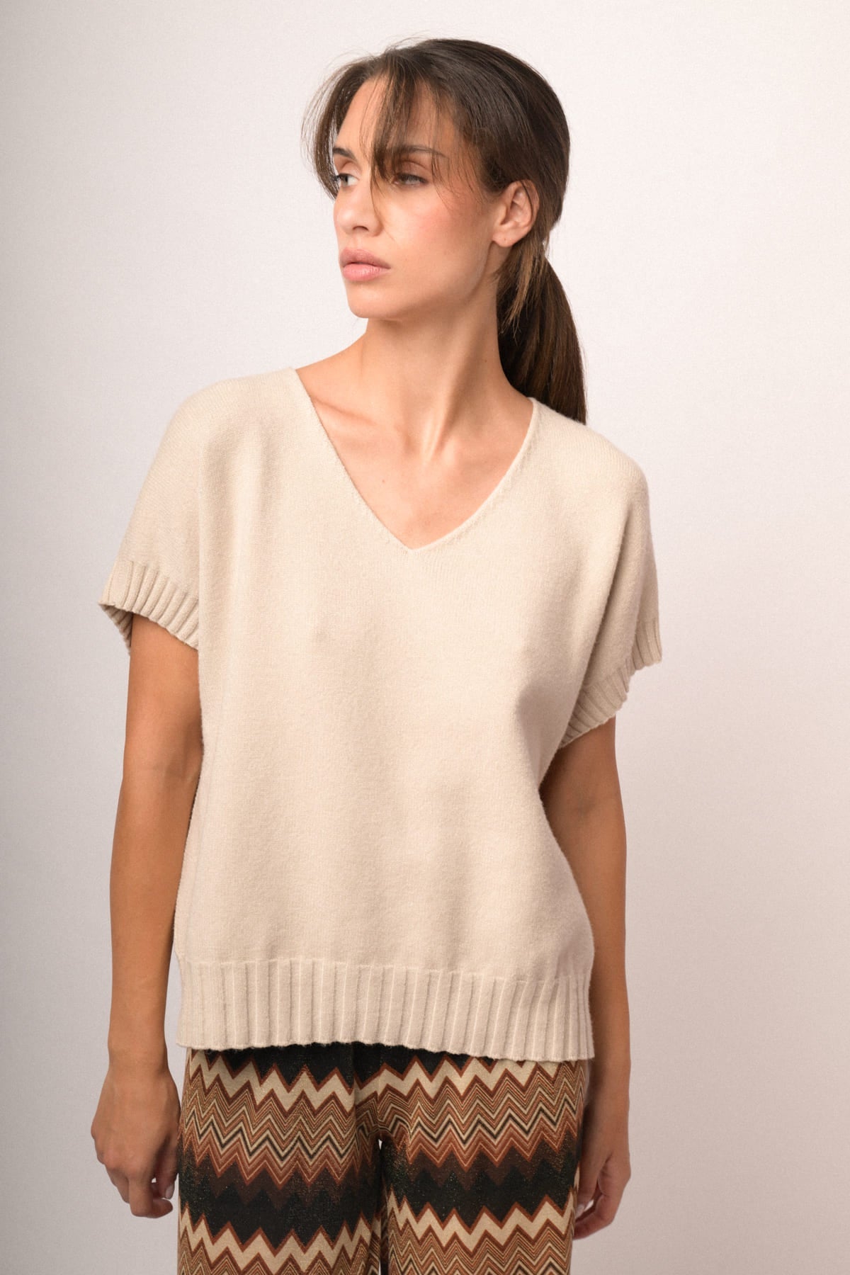 Chaleco de punto beige con escote en V, tejido liso y bajo acanalado.