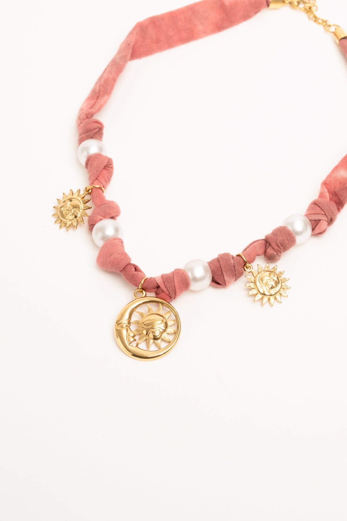 Collar con tejido rosa y colgantes dorados: medallón y soles, con cuentas blancas