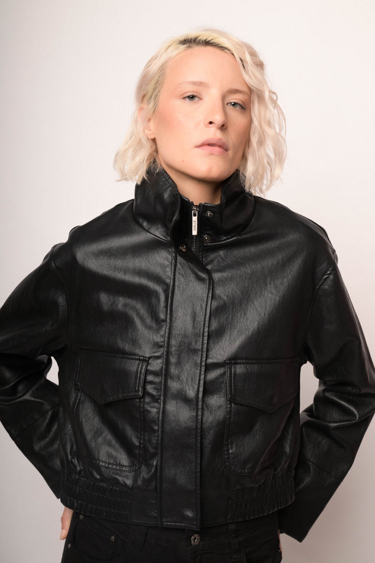 Chaqueta bomber de polipiel negra con cierre frontal y cuello alto, bolsillos laterales.