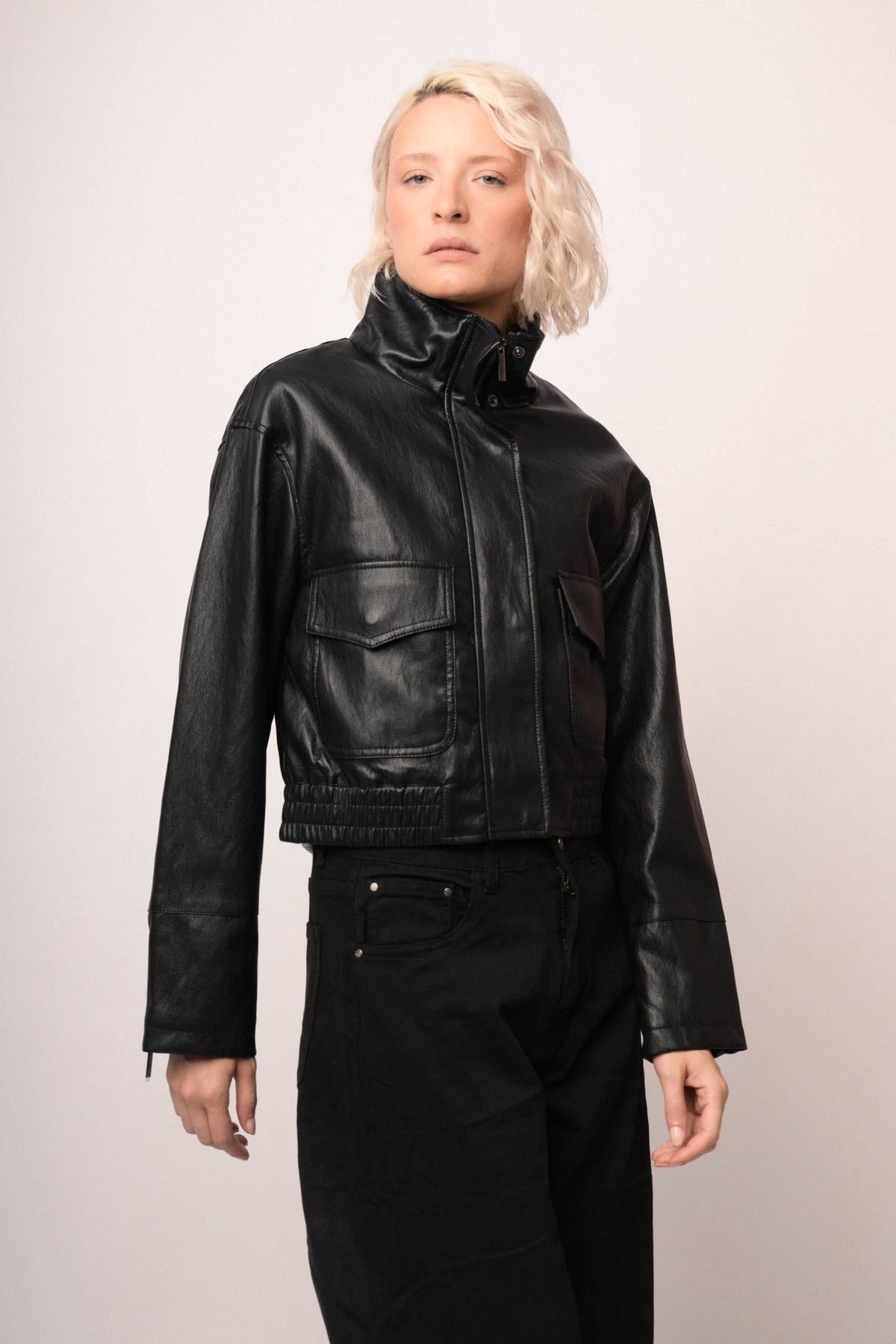 Chaqueta bomber de polipiel negra con cuello alto y bolsillos en el pecho, manga larga.