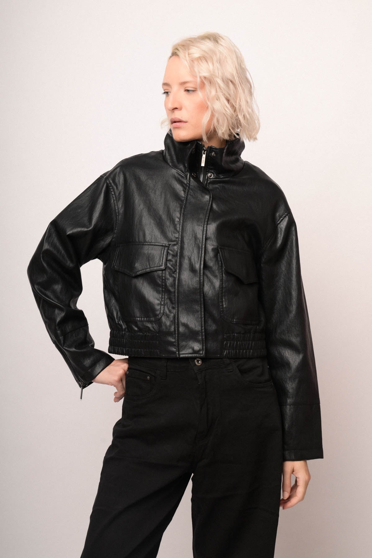 Chaqueta bomber de polipiel negra con cierre frontal y bolsillos laterales, vista lateral.