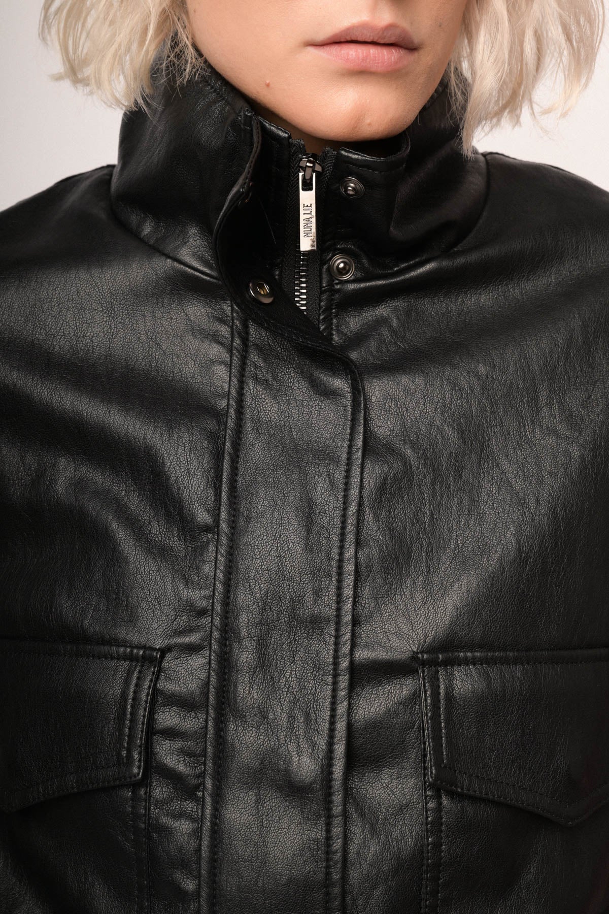 Chaqueta bomber de polipiel negra: cierre frontal y botones del cuello alto, detalle.