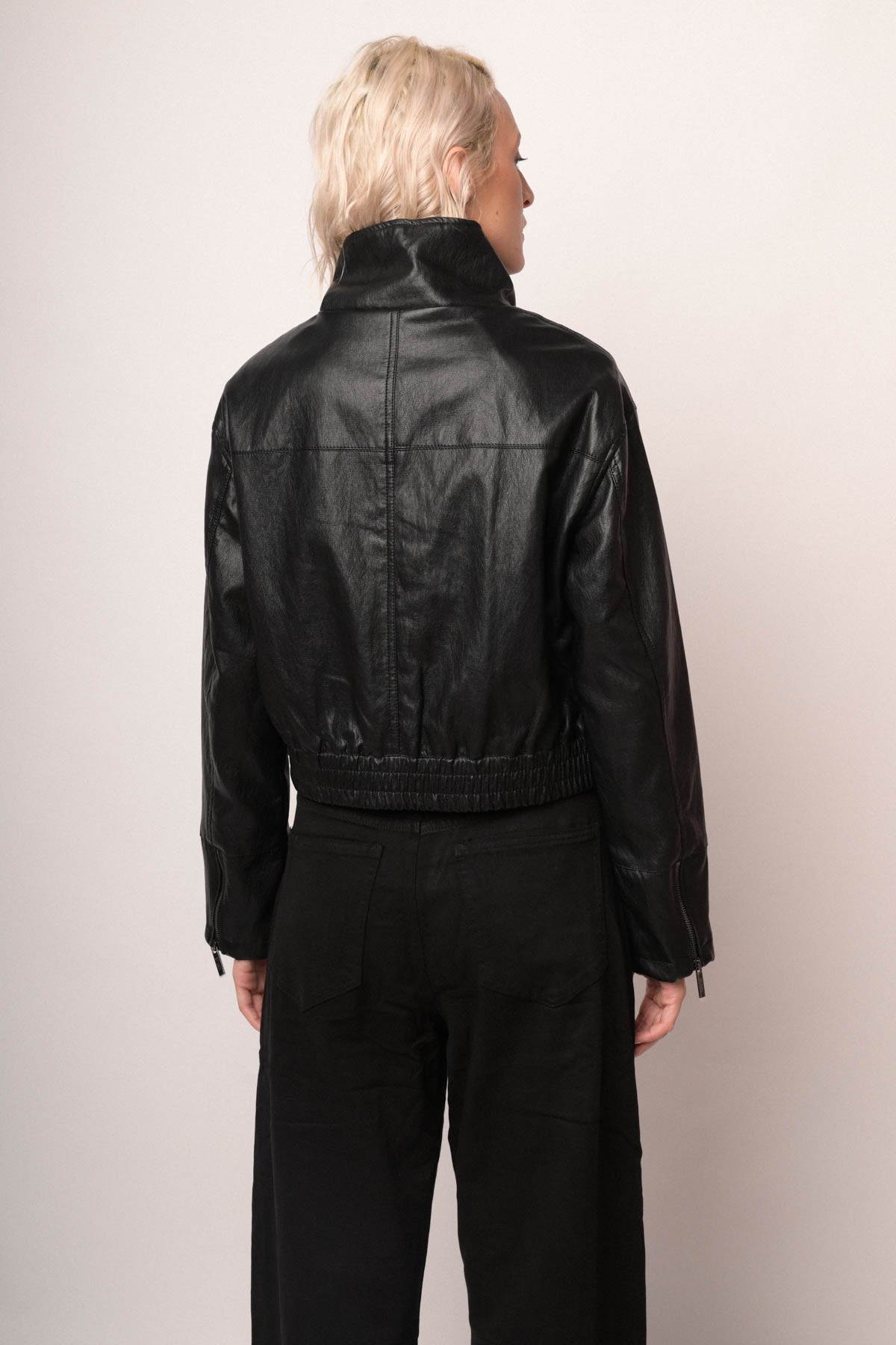 Chaqueta bomber de polipiel negra vista trasera, cuello alto y puños ajustados.